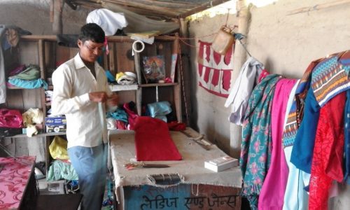 Mr. Khusi Ram Chaudhary, from Thapapur village of Kailali district, taking measurements of the clientele-clothes at his tailoring shop